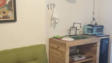 Un espacio habitable compacto con un sofá verde, una kitchenette con tostadora y una lámpara colgante.