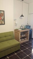 Un espacio habitable compacto con un sofá verde, una kitchenette con tostadora y una lámpara colgante.