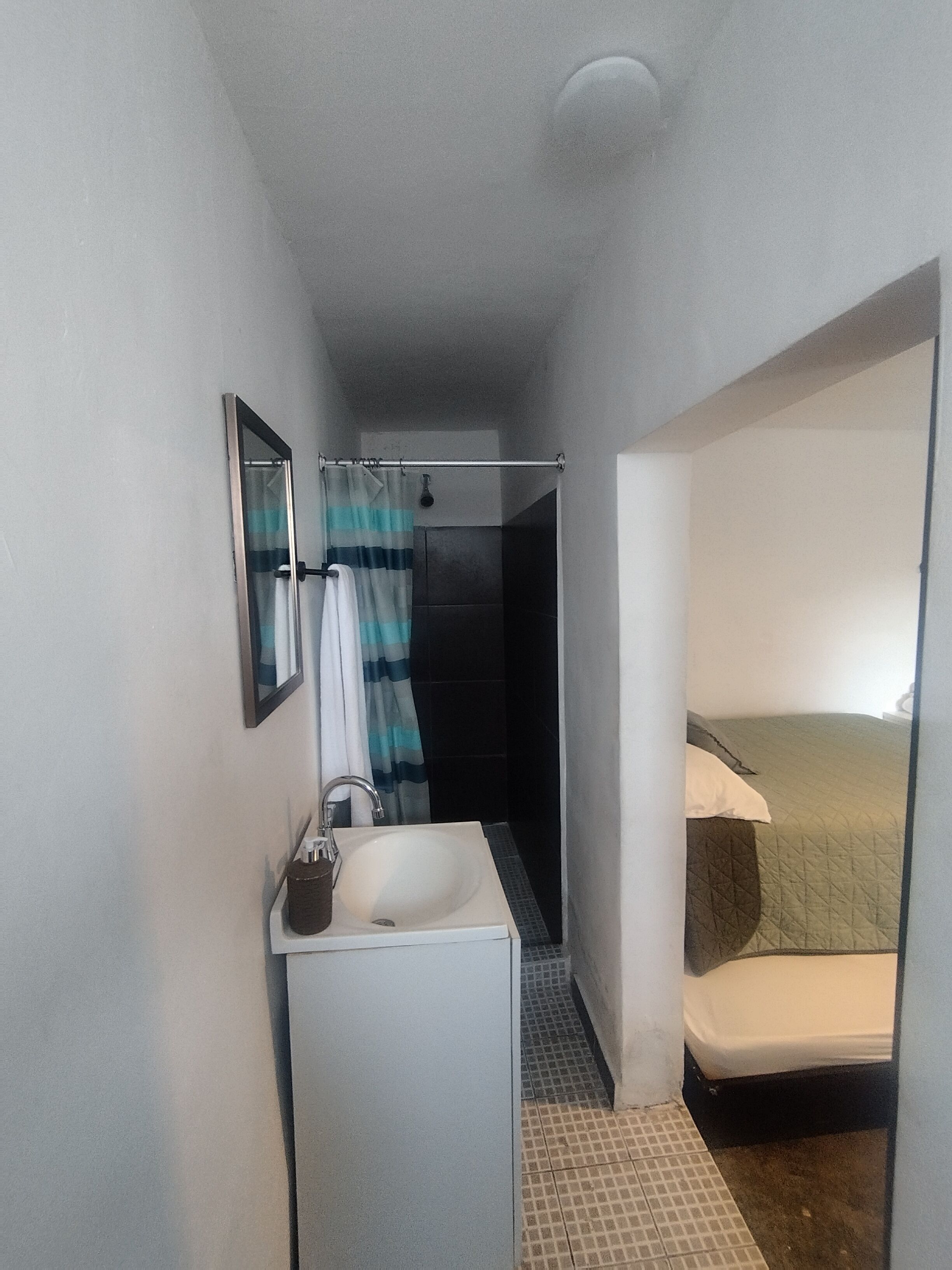 Una habitación pequeña con ducha, lavamanos y cama.