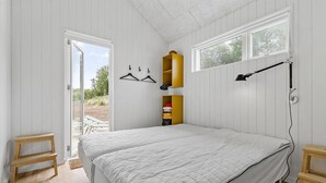 Ein Schlafzimmer mit einem Bett, Holznachttischen, einer Hängelampe und einem Kleiderschrank mit gelber Tür.