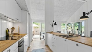Eine moderne Küche mit weißen Schränken, Holzarbeitsplatten und einem großen Fenster mit Blick ins Freie.