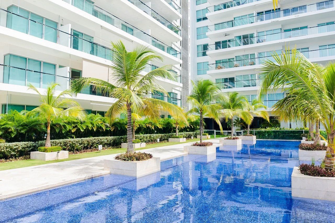 Un hotel moderno con una amplia piscina interior rodeada de palmeras y un jardín cuidado.