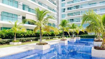 Un hotel moderno con una amplia piscina interior rodeada de palmeras y un jardín cuidado.