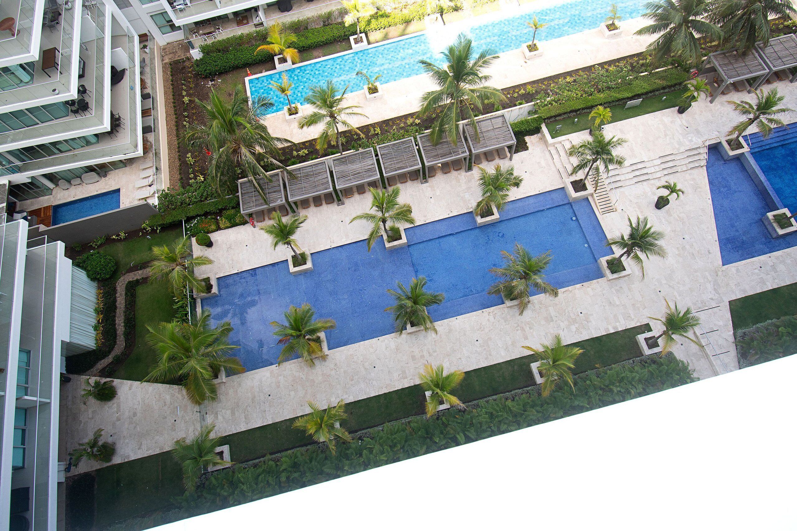 Uma área de piscina no terraço com várias piscinas, palmeiras e espreguiçadeiras.