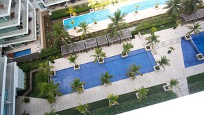Un espace piscine sur le toit, comprenant plusieurs piscines, des palmiers et des chaises longues.