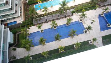 Uma área de piscina no terraço com várias piscinas, palmeiras e espreguiçadeiras.