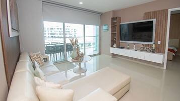 Una sala de estar moderna con una televisión de pantalla plana grande, un sofá, una mesa de centro y un balcón con vistas a edificios.