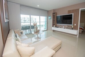 Ein modernes Wohnzimmer mit großem Flachbildfernseher, einer Couch, einem Couchtisch und einem Balkon mit Blick auf Gebäude.