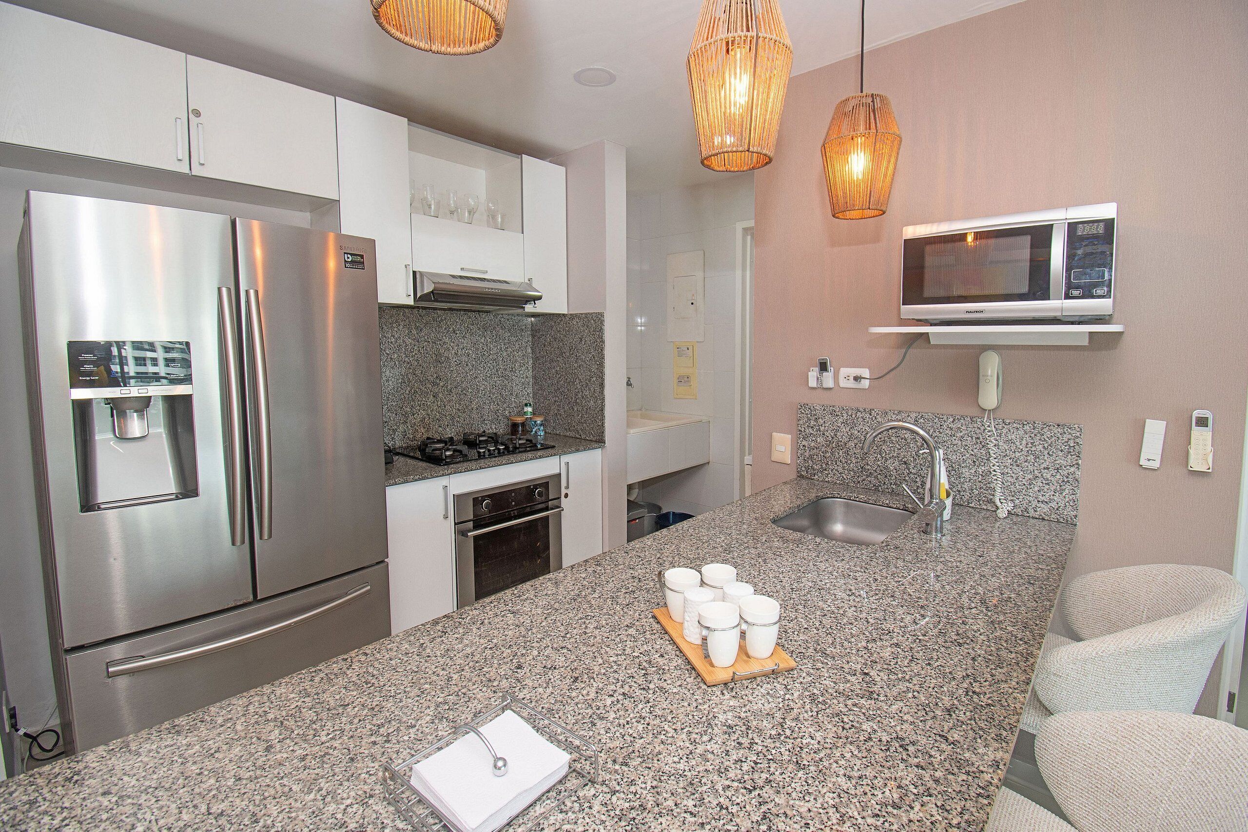 Una cocina moderna con electrodomésticos de acero inoxidable, encimeras de granito e iluminación colgante.
