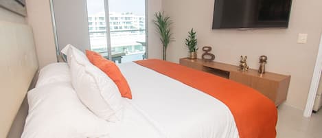 A bedroom with a bed, a TV, a plant, and a wooden dresser.