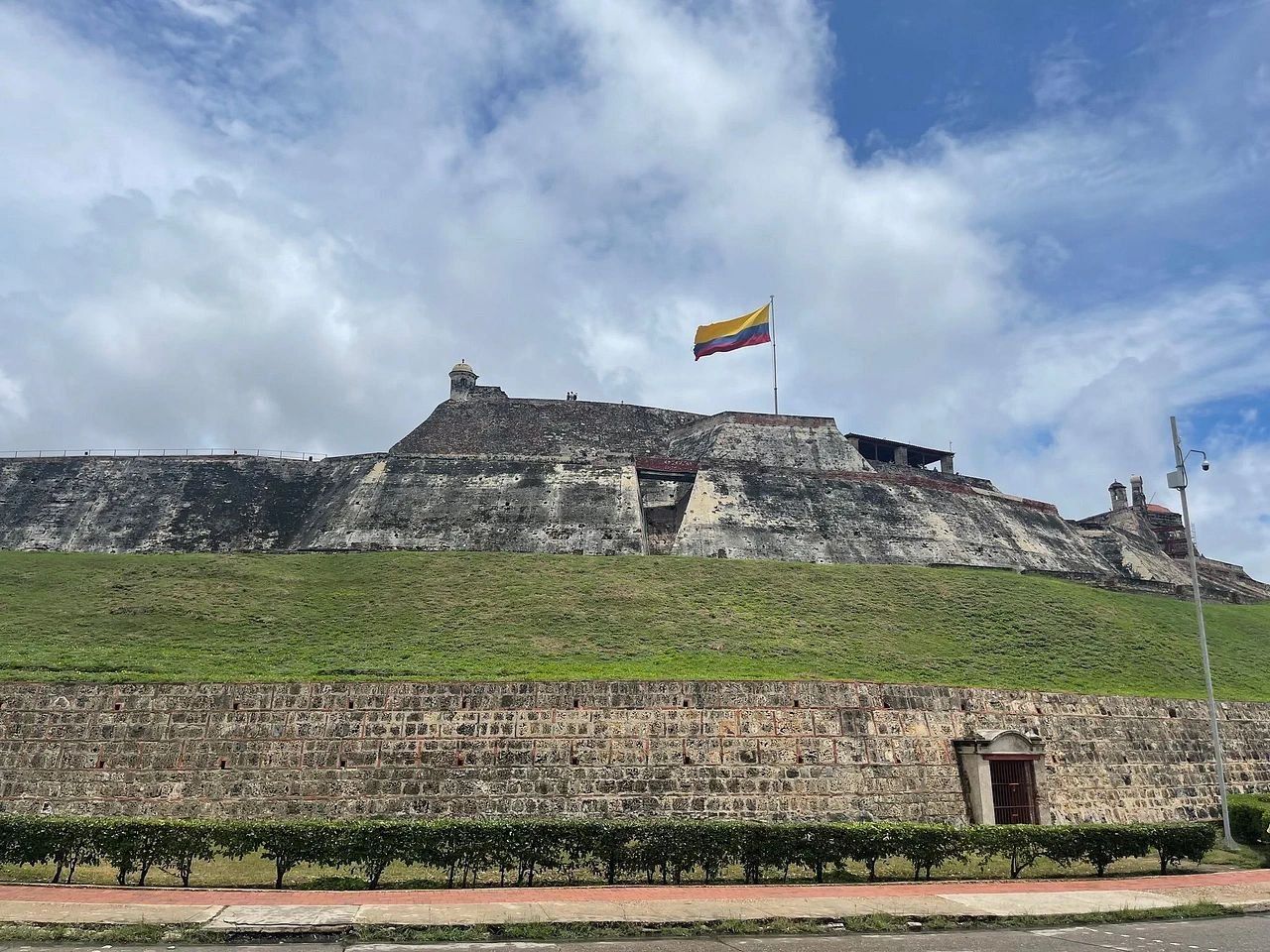 A large fortress-like structure with a flag on top, a stone wall in the foreground, and a clear sky.