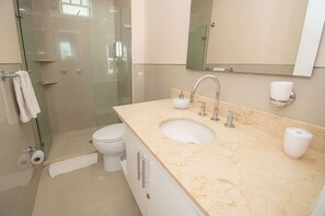 Et moderne badeværelse med en glasbrusekabine, et hvidt toilet, en marmorvask med vandhane og et spejl over spejlskabet.