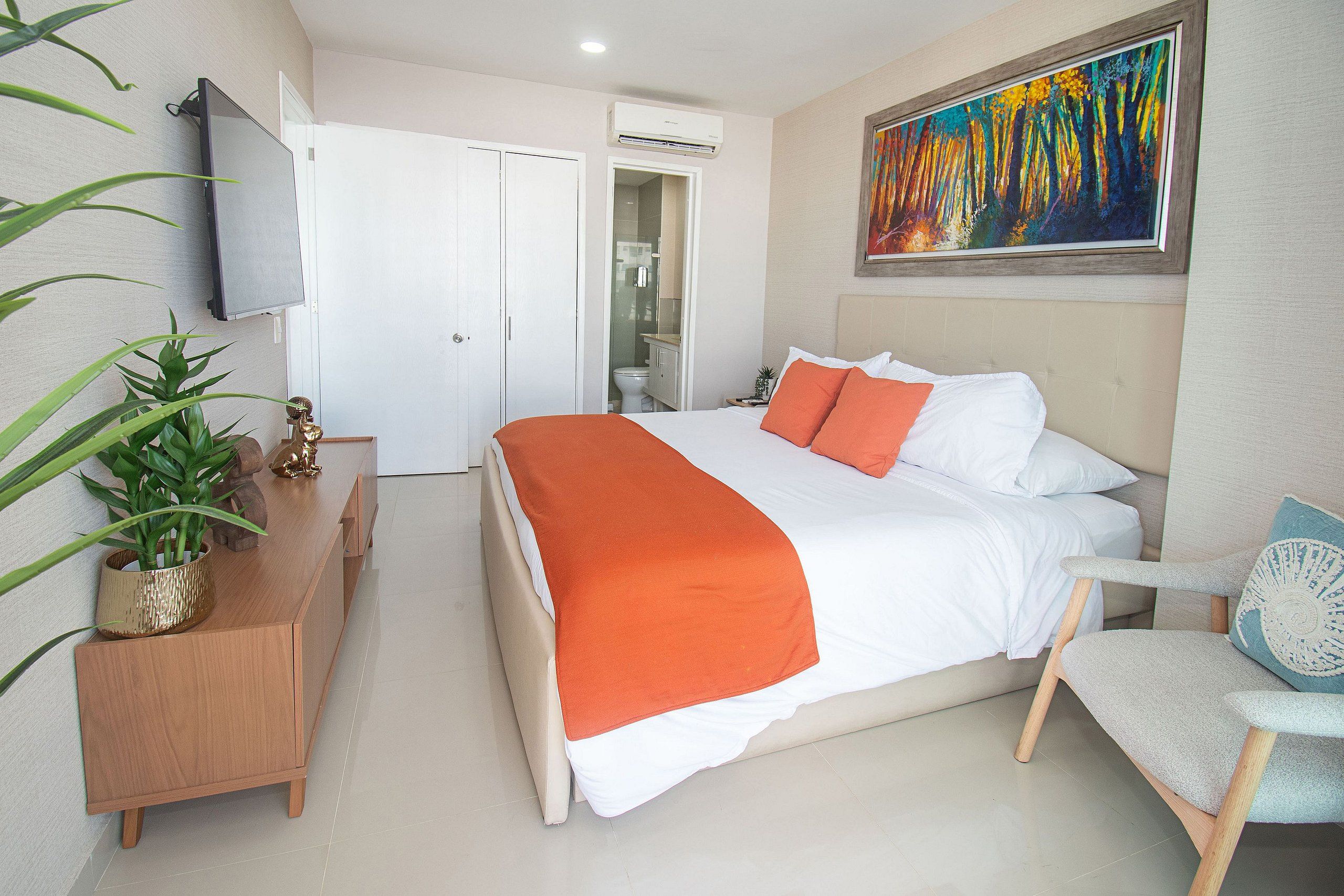 A hotel room with a bed, a desk, a chair, a TV, and a painting on the wall.