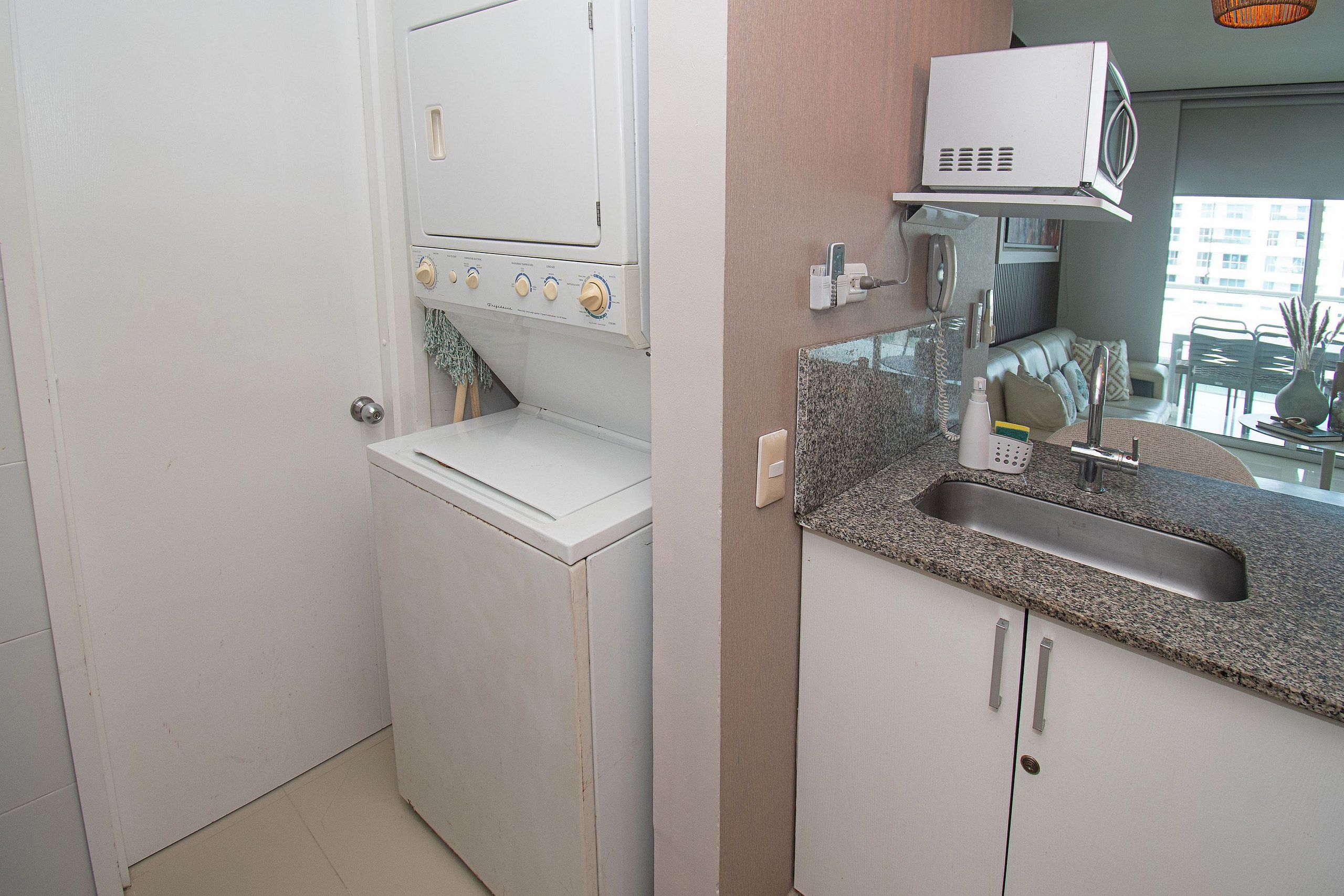 Cocina compacta con lavadora integrada, microondas y lavaplatos de encimera de granito.