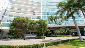 A modern hotel with a curved glass facade, multiple balconies, and lush landscaping including palm trees and well-maintained hedges. - U-GO Edificio Morros Ultra (Cartagena)
