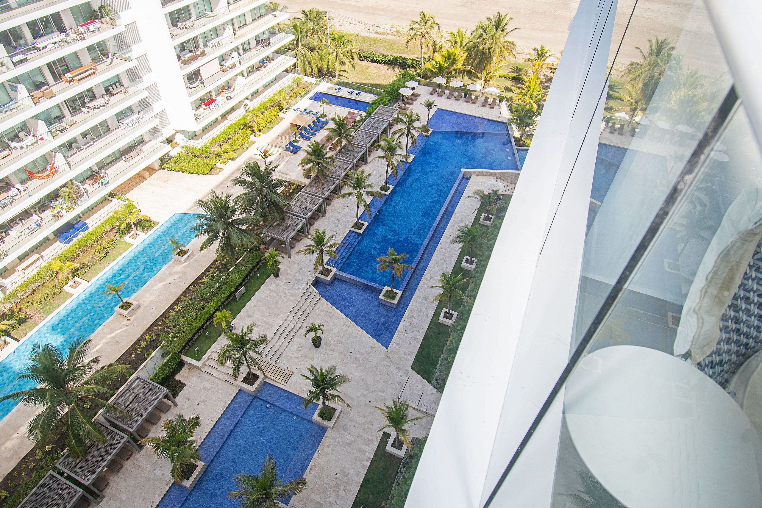 A multi-level hotel with a pool area, including a large central pool and smaller pools, surrounded by palm trees and lounge chairs.