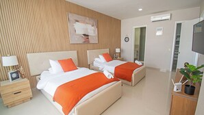 Une chambre d’hôtel avec deux lits, une télévision, une plante et une salle de bain visible à travers une porte ouverte.