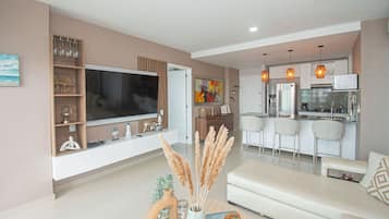 Una sala de estar moderna con un televisor de pantalla plana, un sofá y un comedor con taburetes de bar.