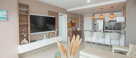 A modern living room with a flat-screen TV, a sofa, and a dining area with bar stools.