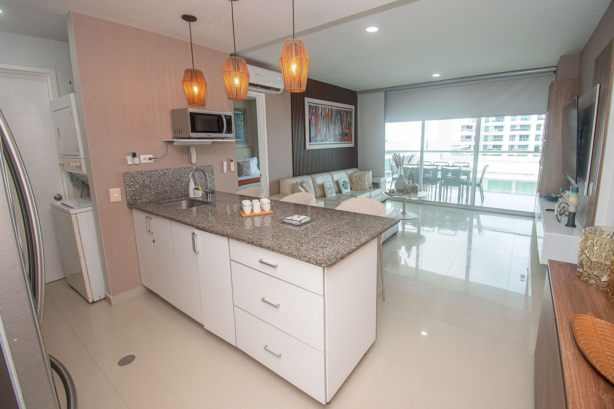 Una cocina moderna con una isla central, luces colgantes y un área de comedor con vistas.