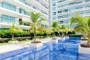 Un hotel moderno con una amplia piscina interior rodeada de palmeras y un jardín cuidado.