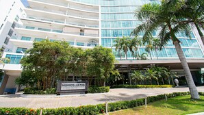 A modern hotel with a curved glass facade, multiple balconies, and lush landscaping including palm trees and well-maintained hedges. - U-GO Edificio Morros Ultra (Cartagena)