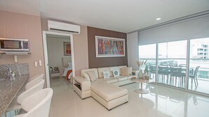 A modern living room with a sofa, a dining area with chairs, a kitchen with a microwave, and a large window with a view. - U-GO Edificio Morros Ultra (Cartagena)