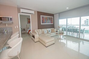 A modern living room with a sofa, a dining area with chairs, a kitchen with a microwave, and a large window with a view. - U-GO Edificio Morros Ultra (Cartagena)