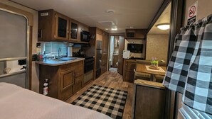 A compact RV kitchen with wooden cabinets, a microwave, stove, and a small dining area with a checkered rug. - RV/camper in terrific Via Madonna property (Englewood)