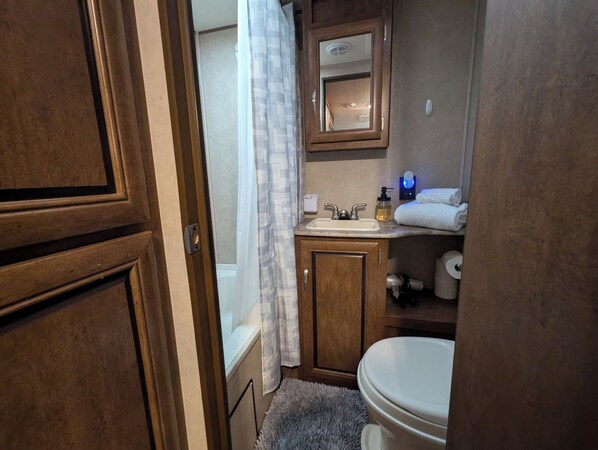 A bathroom with a wooden vanity, a sink, a mirror, a toilet, and a shower curtain.