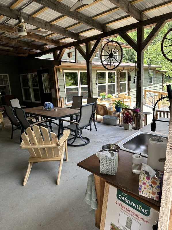 Un patio cubierto con una mesa y sillas de madera, una rueda grande y vista a una casa.