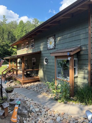 A two-story wooden house with a porch, a large flower mural, and a stone pathway leading to the entrance. - Cabin W/ Private Pond, Fishing, Peaceful Views, Quiet Smokies Retreat (Sevierville)