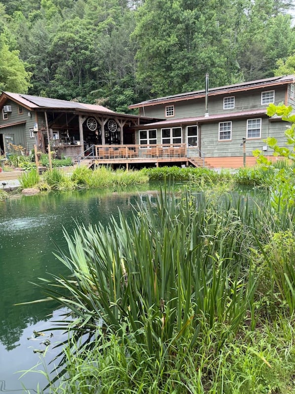 A rustic cabin with a porch and a pond in front.