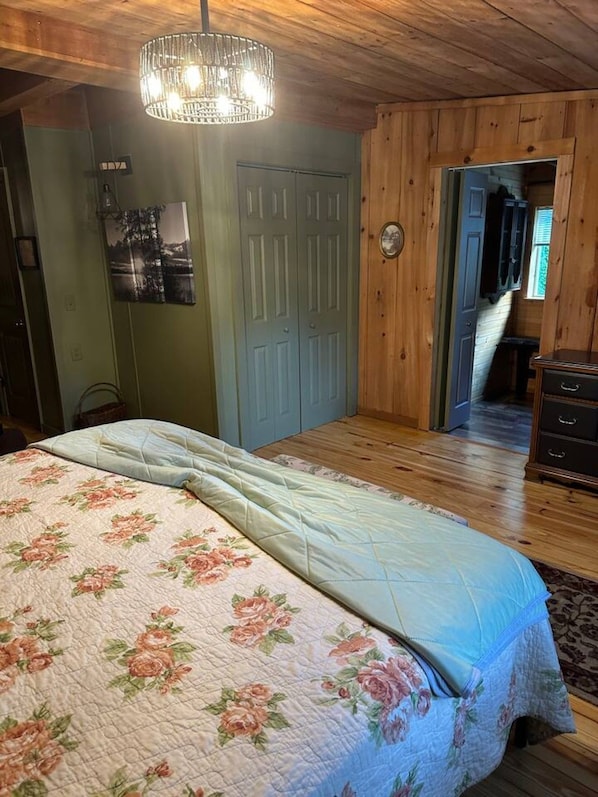 A bedroom with a bed, a chandelier, wooden walls, a door, and a dresser.