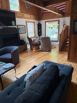 A cozy cabin interior with a fireplace, a sofa, a dining table, and a staircase.