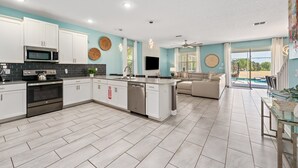 Een moderne keuken met witte kasten, een magnetron, fornuis en vaatwasser. Er is een eethoek met een glazen tafel en stoelen.