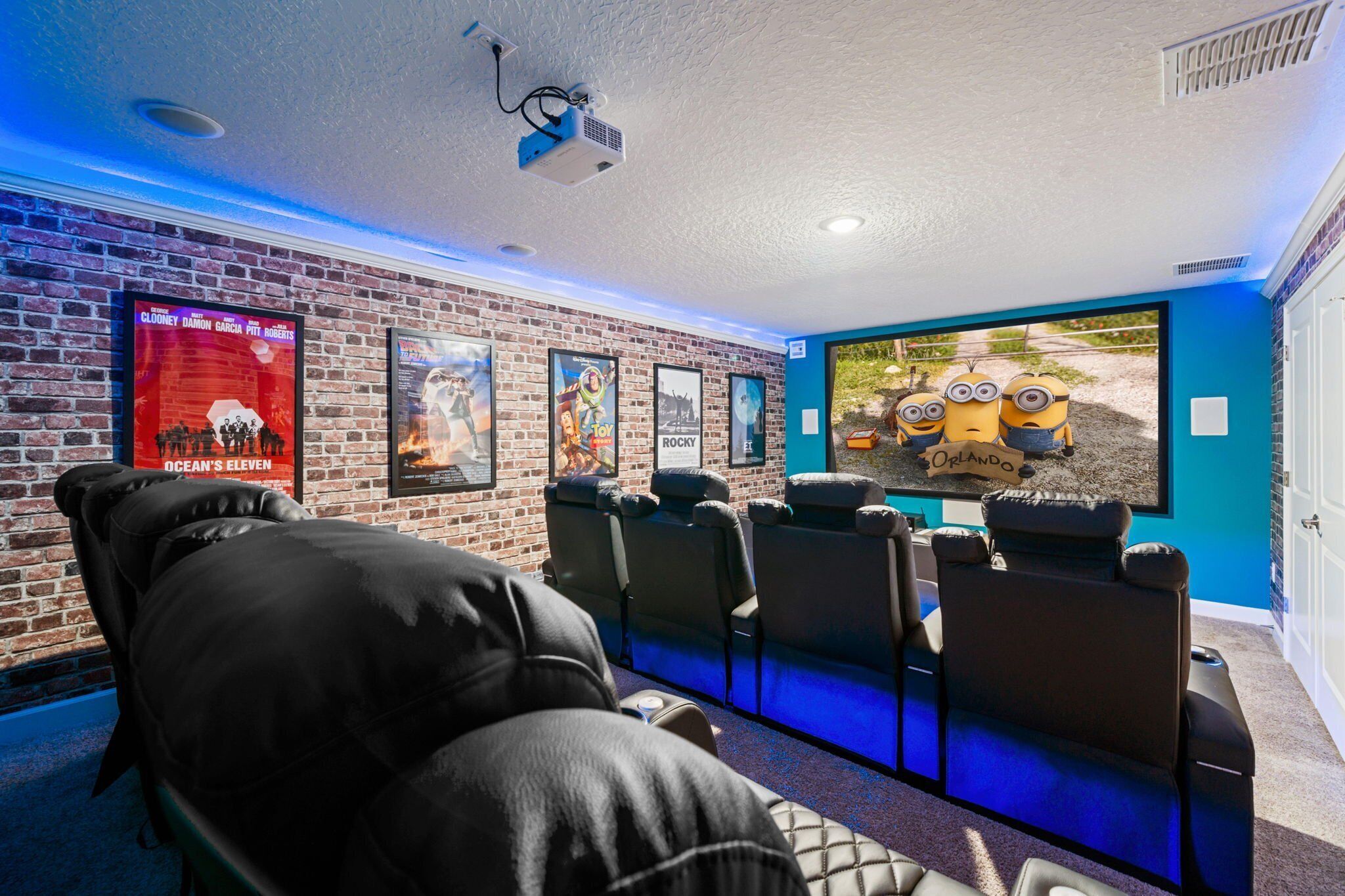 A home theater room with a brick wall, multiple movie posters, and a large screen displaying Minions.