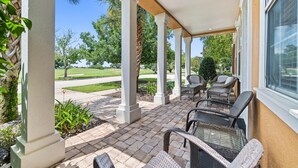 A covered patio area with wicker furniture, white columns, and a view of a well-maintained lawn and trees. - Theater Room | Games Area | Kids Themed Bedrooms | Private Pool (Kissimmee)