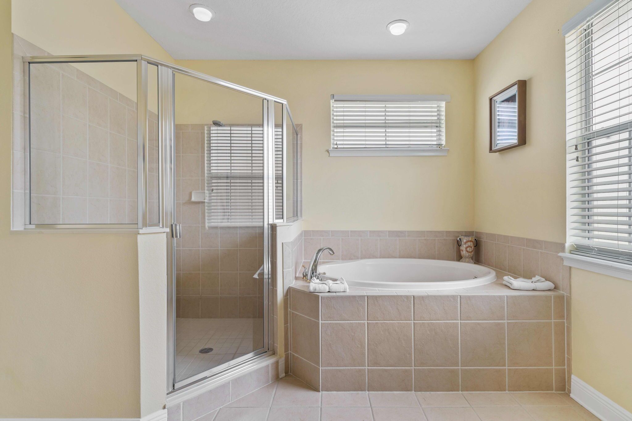 Une salle de bain avec une douche à parois de verre, une baignoire et une fenêtre équipée de stores.