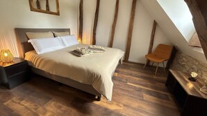 Une chambre à coucher avec un lit, des tables de chevet, une chaise et un mur avec une poutre en bois.