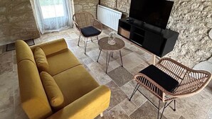 Un salon confortable avec un canapé, deux fauteuils en osier, une table basse et un téléviseur.
