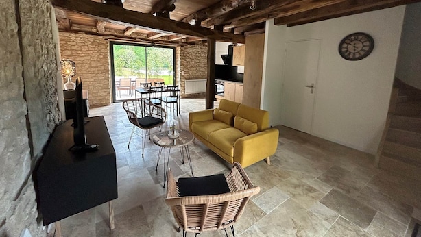 Un grand salon avec un canapé jaune, une table à manger avec des chaises, un téléviseur et un mur en pierre.