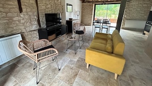 Un salon chaleureux avec des murs en pierre, une télévision, un canapé et une table à manger.