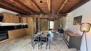Une cuisine rustique avec des poutres en bois, un coin repas avec une table et des chaises, et un mur en pierre.
