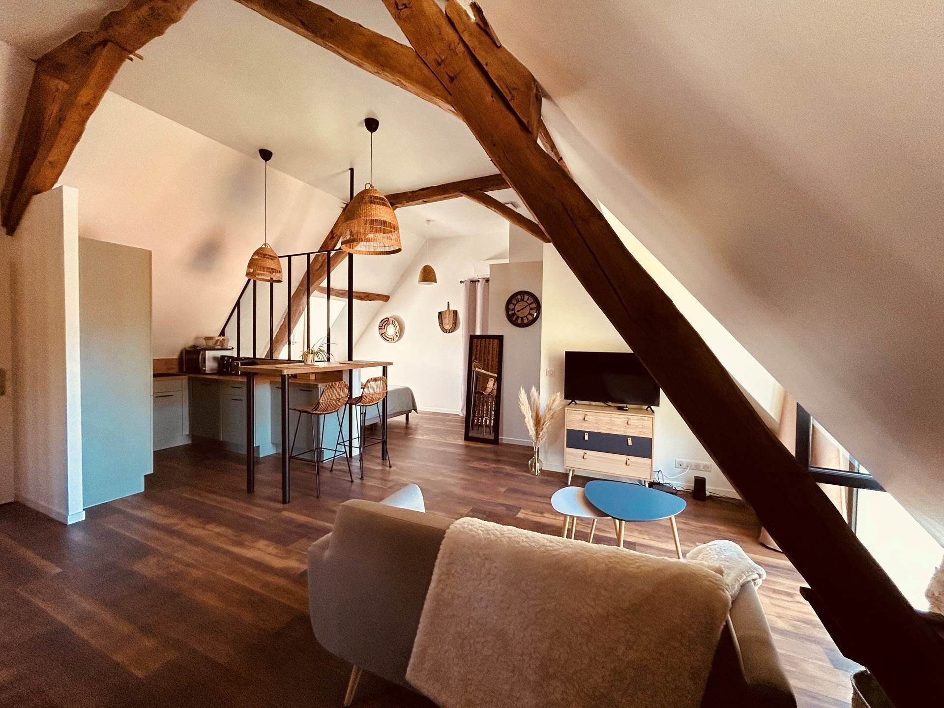 A loft-style living space with exposed wooden beams, a dining area with wicker pendant lights, a sofa, and a small blue table.