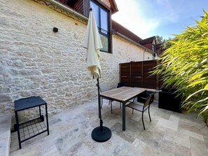 Eine Terrasse mit Steinplatten, einem Tisch, Stühlen, einem kleinen Beistelltisch und einem Blumentopf.