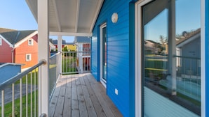 Une façade bleue, une terrasse en bois, une porte en verre et une rambarde en métal.