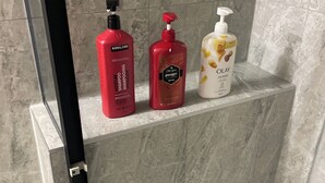 Ein Badezimmer mit Marmorwand und einem Regal mit drei Flaschen Kirkland und Old Spice Duschgel.