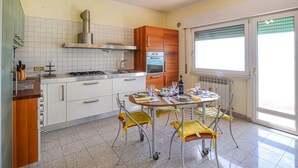 A modern kitchen with white cabinets, a gas stove, an oven, and a window with blinds. - 2 bedroom cozy apartment in Orbetello (Orbetello)