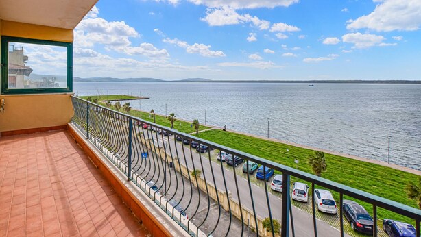 A balcony with a view of a calm body of water, a parking area with cars, and a distant shoreline. - 2 bedroom cozy apartment in Orbetello (Orbetello)